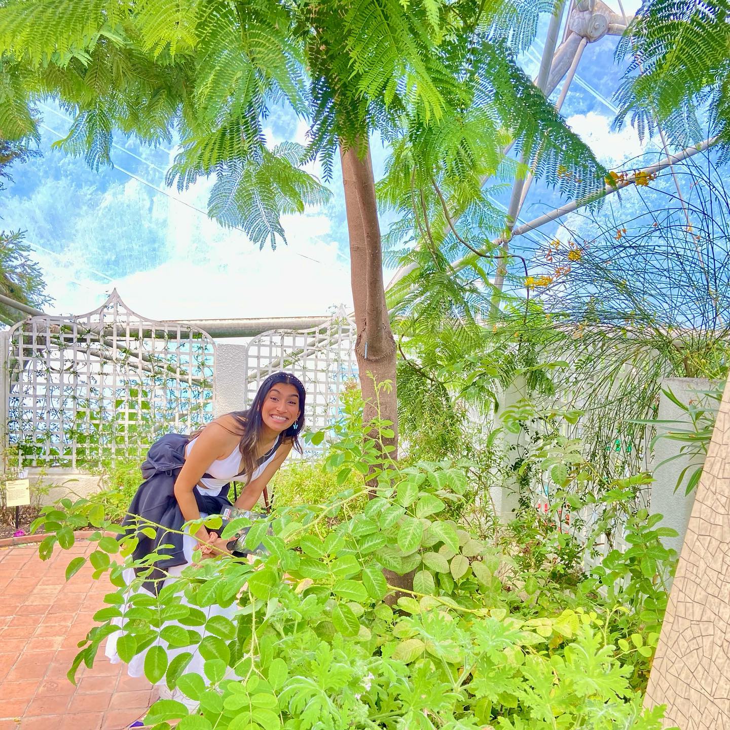 Dr Deesha beaming under a jacaranda tree in a glasshouse garden