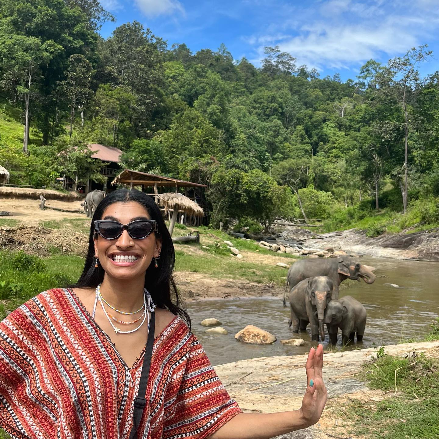 Dr Deesha waving beside elephants bathing in a Chiang Mai river