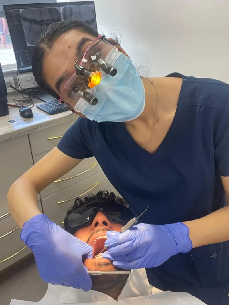 Dr Deesha in loupes and mask, working on a reclined patient